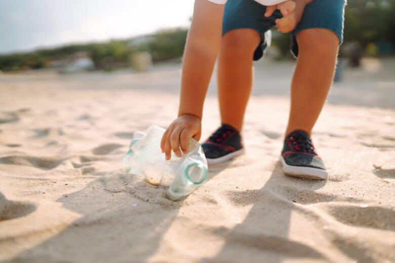 Criança recolhendo garrafa deComo a educação ambiental transforma escolas, comunidades costeiras e o turismoplástico na praia/Educação ambiental